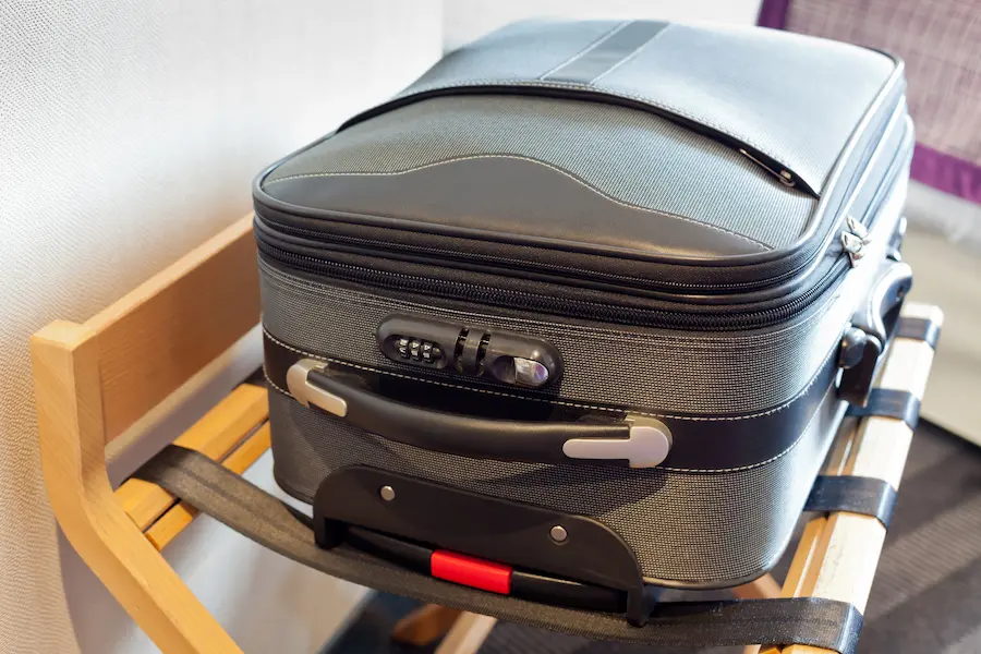 A gray suitcase on a suitcase rack to keep it off the ground in a hotel room.
