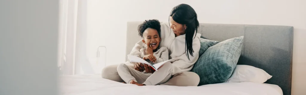 A mother and daughter laughing while looking at a book on bed in a pest-free New York home
