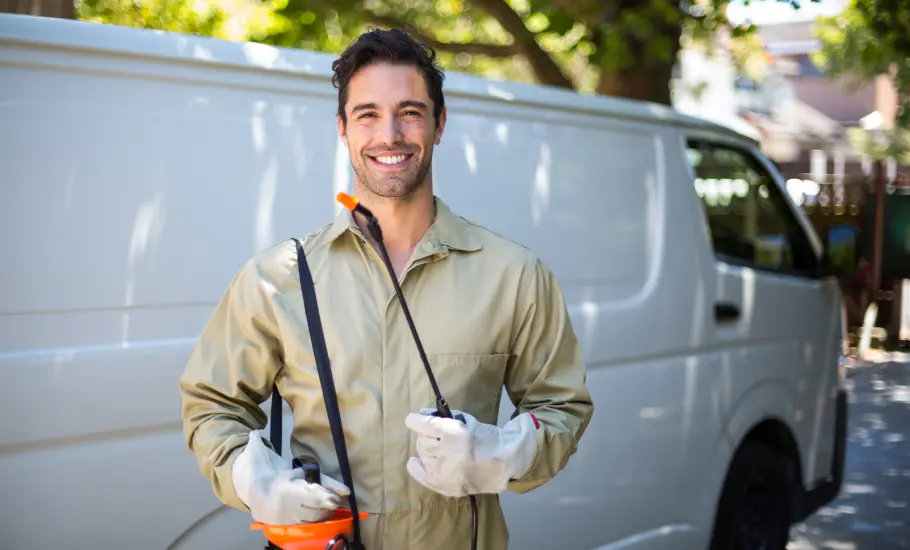 Professional pest technician standing with gear near van after pest application in New York